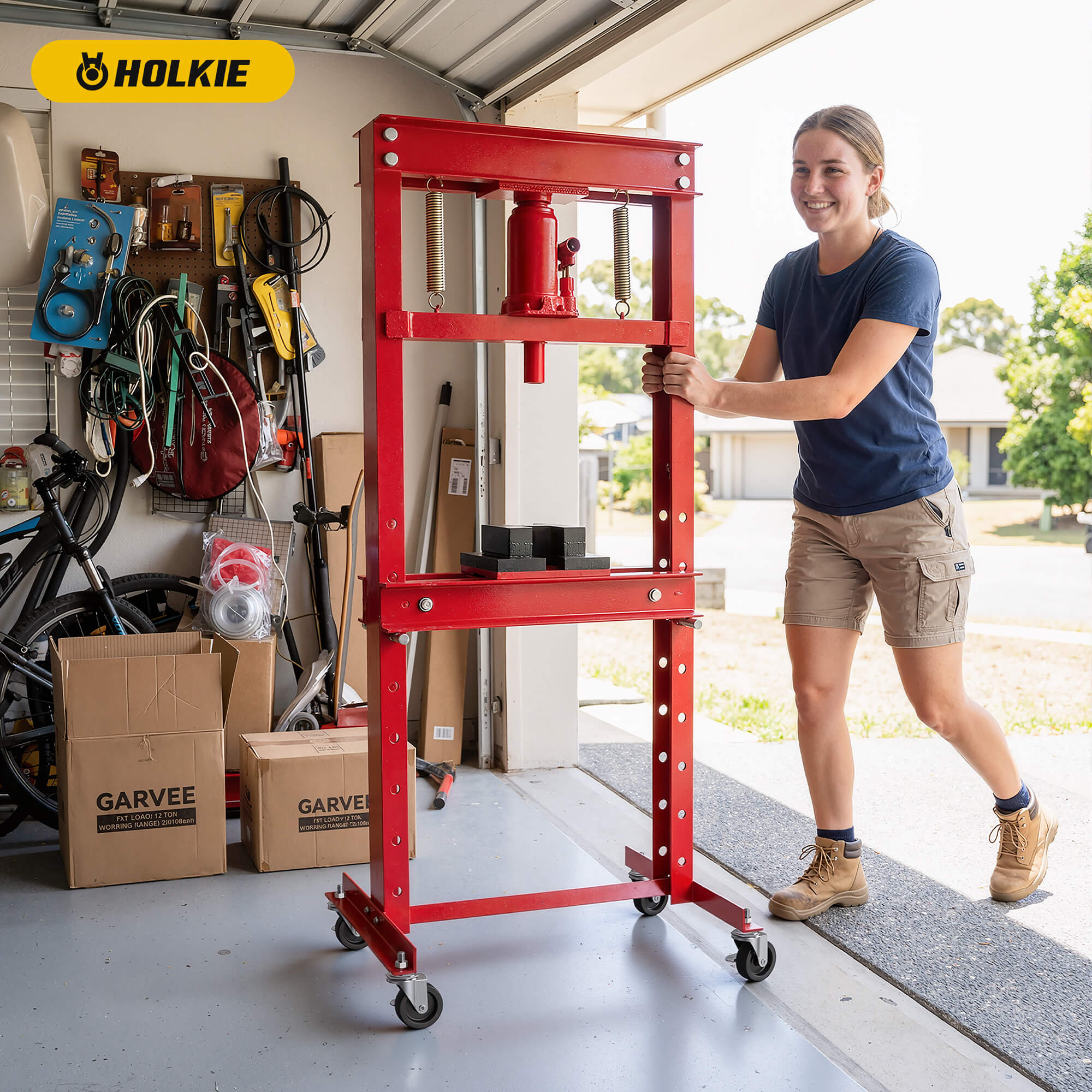 Person moving a heavy red hydraulic shop press with HOLKIE casters in a garage organized with tools
